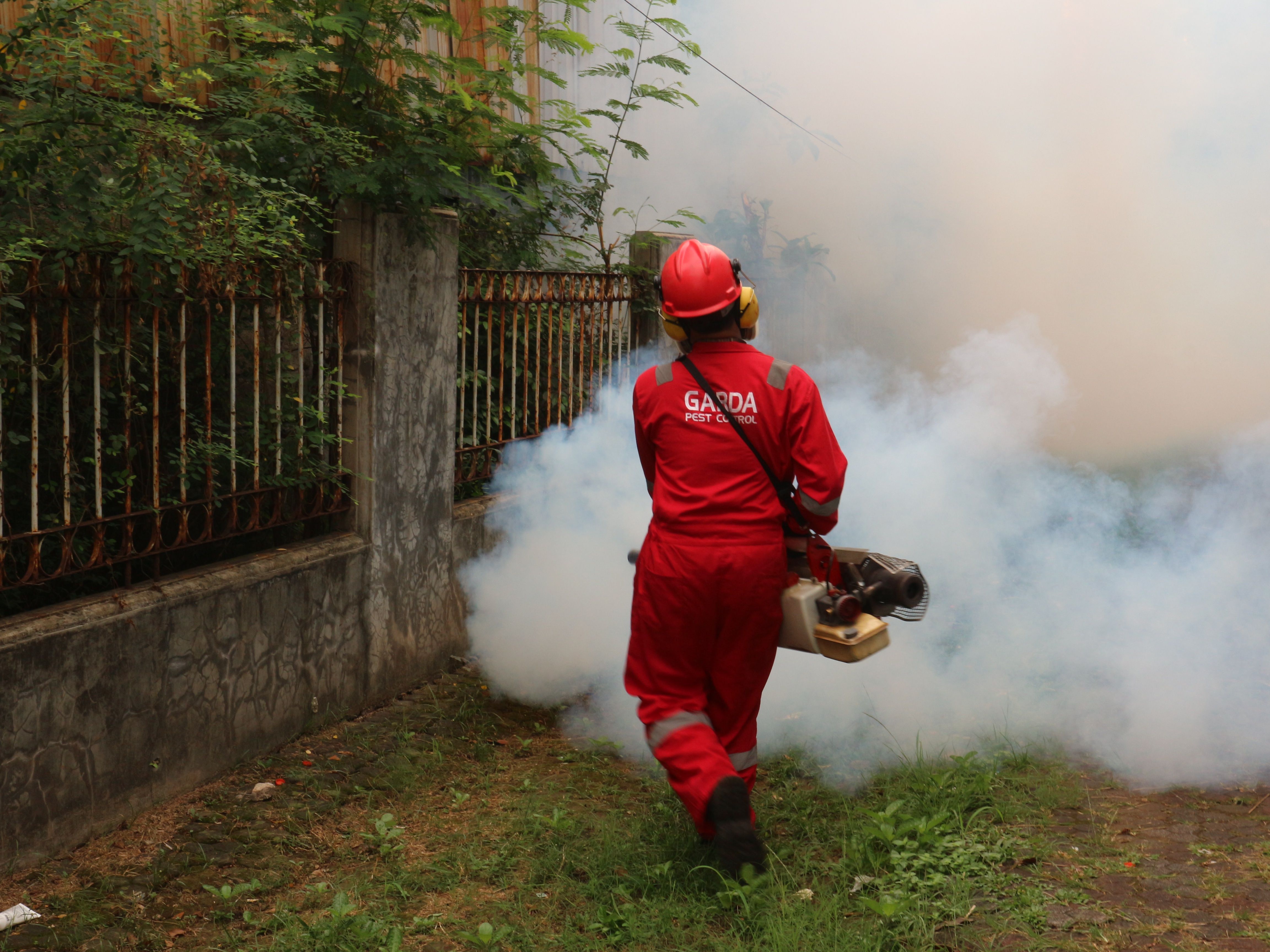 Pest control technician fogging a yard in branded coveralls
